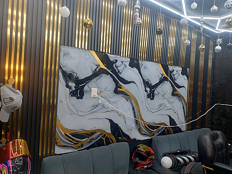 Mural de mármol blanco con vetas negras y doradas sobre dos sillones grises, entre muros de listones dorados