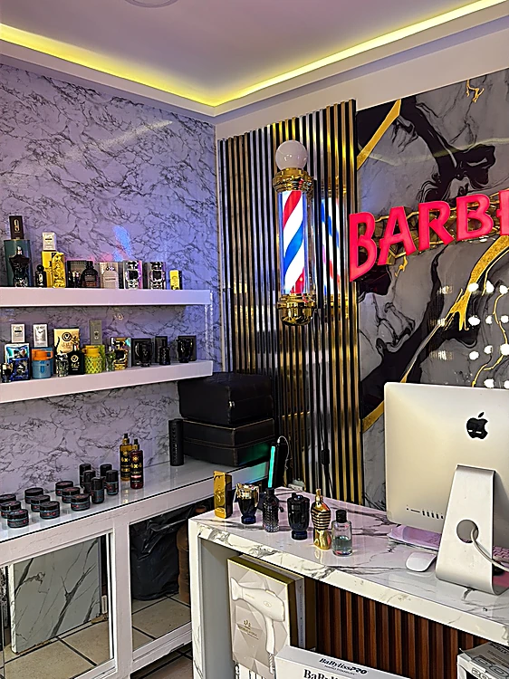 Repisas de mármol con lociones, ceras y productos para barba, junto a un poste de barbero iluminado y el letrero rojo